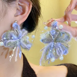 Vista detallada de pendientes de flores de lana púrpura hechos a mano con perlas blancas