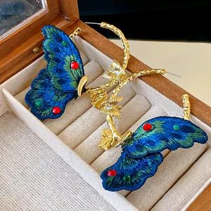 Close-up of embroidered blue butterfly hoop earrings with red and green gemstones