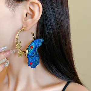 Close-up of elegant gold hoop earring with blue embroidered butterfly detail on model