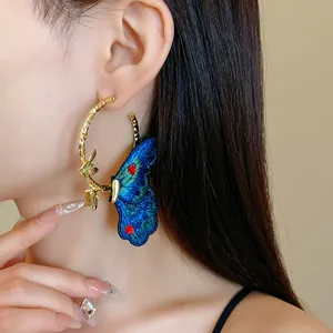 Close-up detail of elegant embroidered blue butterfly gold hoop earring on model