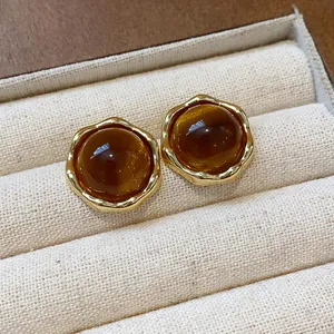 Macro view of amber resin stud earrings with gold scalloped borders on linen