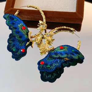 Detailed macro shot showing the intricate blue embroidery and crystals on butterfly hoop earrings.