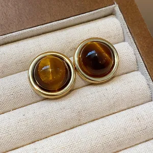 Macro view of gold-plated stud earrings with shimmering brown resin cabochons