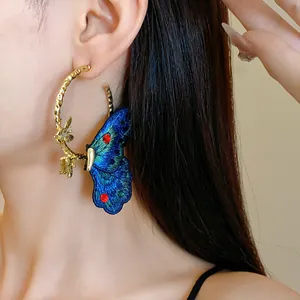 Close-up detail of blue embroidered butterfly hoop earring worn on model