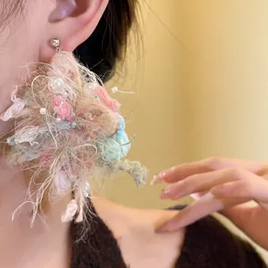 Vista detallada de pendientes de flores de lana con perlas en la oreja de una modelo.