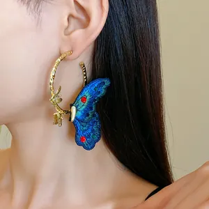 Detailed view of gold textured hoop earring with intricate blue embroidered butterfly.