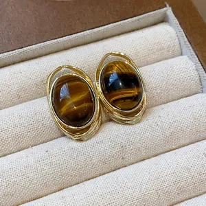 Close-up of elegant gold-plated stud earrings with brown resin stones in a jewelry box