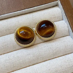Detail view of round resin stud earrings with golden rope border in Maillard style