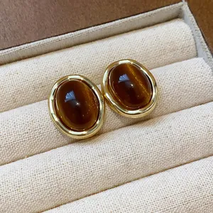 Detailed close-up of elegant gold-plated resin stud earrings in rich amber brown tone