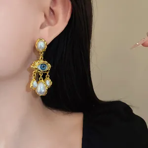 Detail view of vintage gold-tone eye motif earrings with elegant faux pearl tassels.