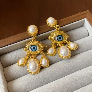 Detailed macro view of vintage gold-tone evil eye earrings featuring elegant faux pearls.