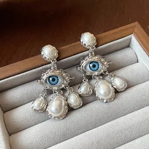 Detail of vintage silver-tone earrings featuring a blue eye motif and pearl drops