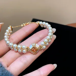 Close-up of double-strand pearl bracelet with amber zircon centerpiece and gold plating.