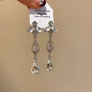 Gros plan détaillé de boucles d'oreilles pendantes argentées avec cristaux roses et transparents.
