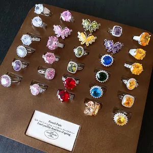 Selezione di vari anelli con zirconi colorati esposti su una base di legno marrone.