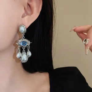 Detailed close-up of vintage palace style silver earring with blue eye motif and pearl tassels