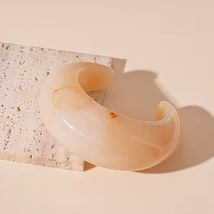 Macro detail view of chunky beige resin bangle with amber marble swirls on a stone block.