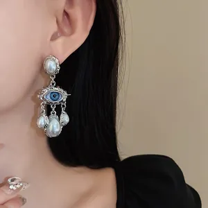 Close-up of a vintage evil eye earring with molten silver texture and pearl tassels