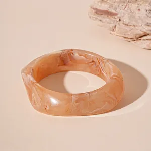 Close-up of an irregular resin bangle with beige marble texture and unique wavy design.