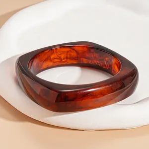 Close-up of a marbled brown resin bangle with a unique irregular square shape decoration