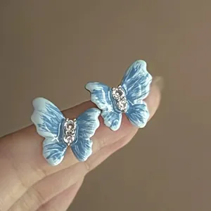Close-up of blue butterfly stud earrings with oil drop finish and sparkling rhinestones.