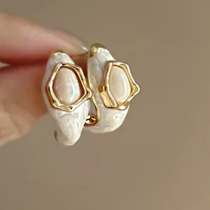 Detailed close-up of geometric enamel earrings with white pearlescent texture and gold finish