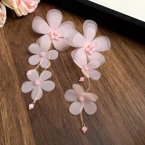 Dettaglio di orecchini a nappa con fiori in chiffon rosa e sottili catene dorate