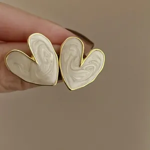 Macro close-up view of heart-shaped earrings featuring swirling cream enamel and gold frame