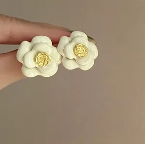 Macro view of elegant white camellia flower stud earrings featuring a gold rose center detail