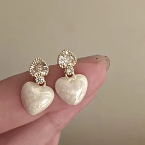 Detailed view of cream enamel heart earrings featuring gold base and sparkling zircon stones