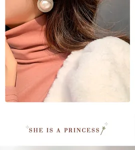 Elegant oversized pearl earrings worn with a pink sweater and white coat, detail shot.