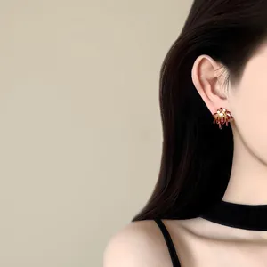 Model wearing firework-shaped stud earrings with dark red enamel and zircon detail