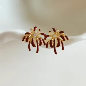 Detailed view of gold firework stud earrings with deep red enamel and clear zircons.