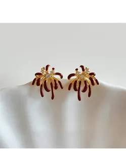 Close-up detail of firework-shaped gold-plated earrings with red enamel and zircons