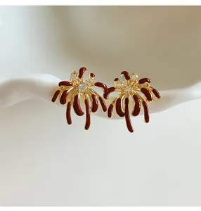 Close-up detail of 18k gold plated firework stud earrings with red enamel and zircon