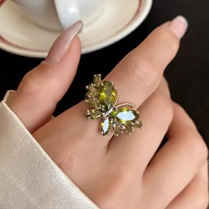 Primo piano di un elegante anello a farfalla in zircone verde indossato su un dito, sfondo morbido