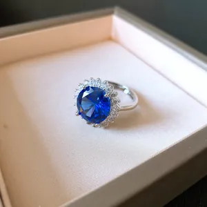 Dettaglio macro di un anello in zircone blu tondo con alone di pietre chiare nella scatola.