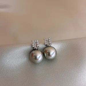 Close-up detail of elegant gray pearl stud earrings with crystal accents on silk satin