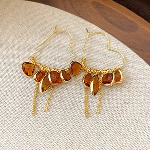 Close-up of 18K gold plated heart earrings with amber stone tassels and chains.