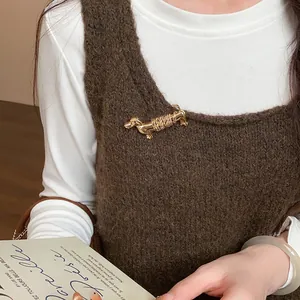 Gros plan d'une broche chien teckel dorée épinglée sur un pull en maille marron.