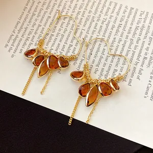 Close-up of elegant 18K gold plated heart-shaped earrings with amber resin teardrop tassels.