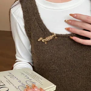 Détail d'une broche chic en forme de teckel doré épinglée sur un gilet en maille marron