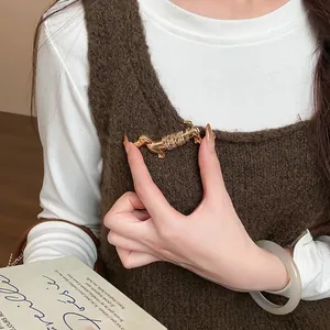 Vue détaillée de la broche teckel dorée épinglée sur un gilet en maille marron.