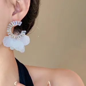 Primo piano di orecchini circolari in zircone con petali bianchi su modella.