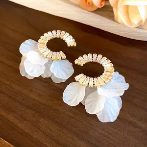 Dettaglio di orecchini a cerchio dorati con zirconi brillanti e petali di fiori bianchi.