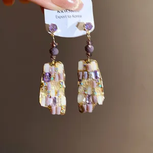Primo piano di orecchini vintage dorati con pendenti a mosaico in viola e bianco.