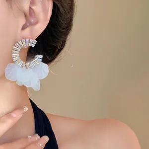 Dettaglio ravvicinato di orecchini a cerchio in zircone con eleganti petali bianchi indossati