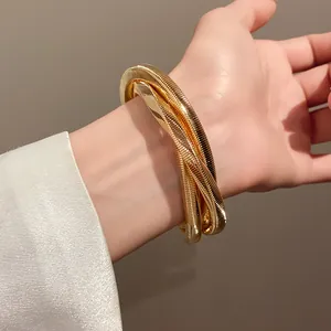 Detailed view of a thick gold-toned metallic twisted swirl bangle bracelet worn on a wrist
