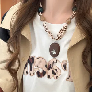 Détail du collier foulard en soie léopard avec pendentif ovale marron sur modèle.