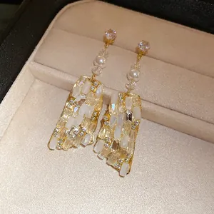 Dettaglio di orecchini vintage dorati con pendenti in vetro a mosaico e accenti di perla